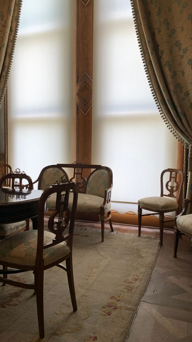 Vintage interior with antique furniture set by large ornate windows with luxurious curtains.