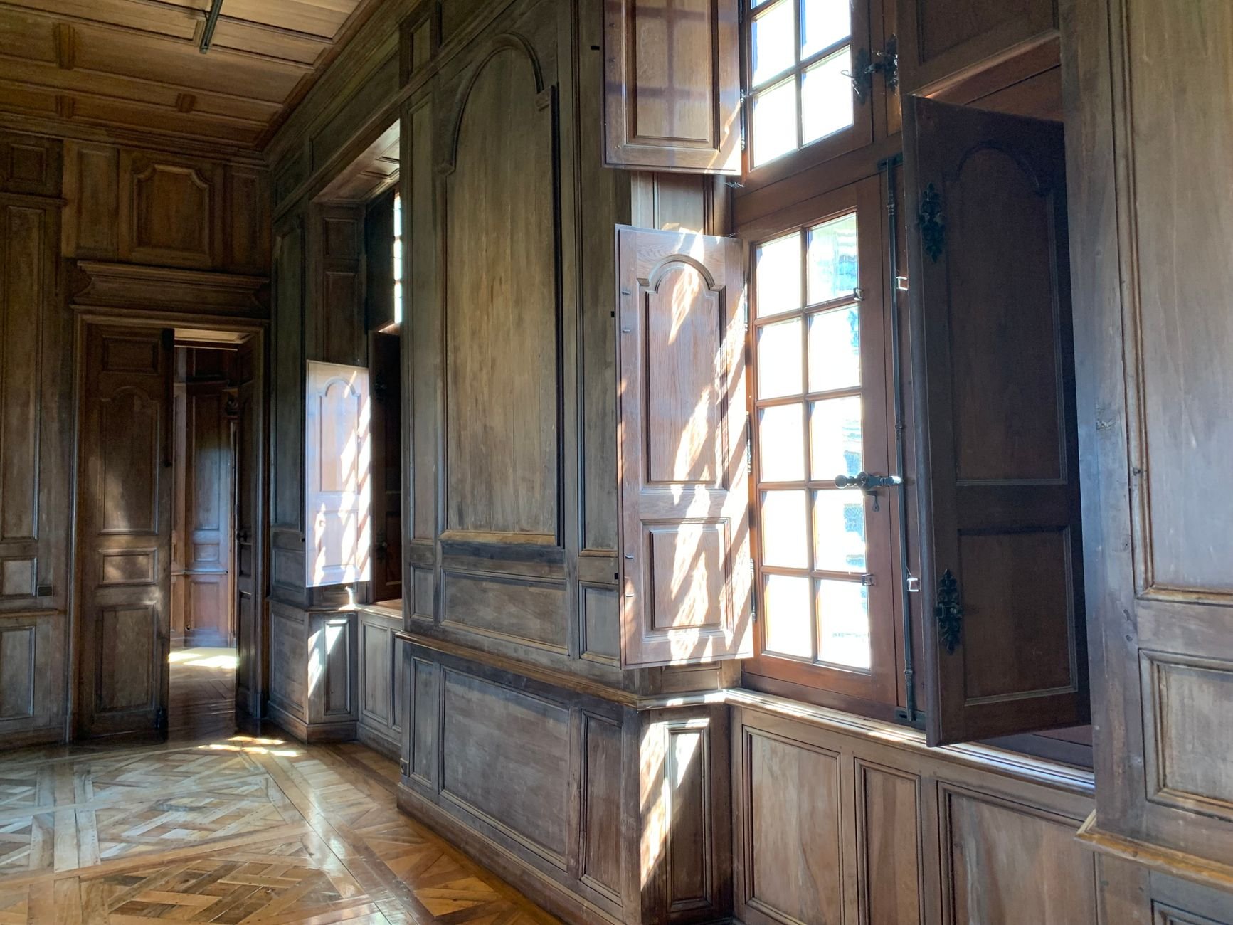 Sunlit interior of a French château with ornate windows, classic woodwork and stone.