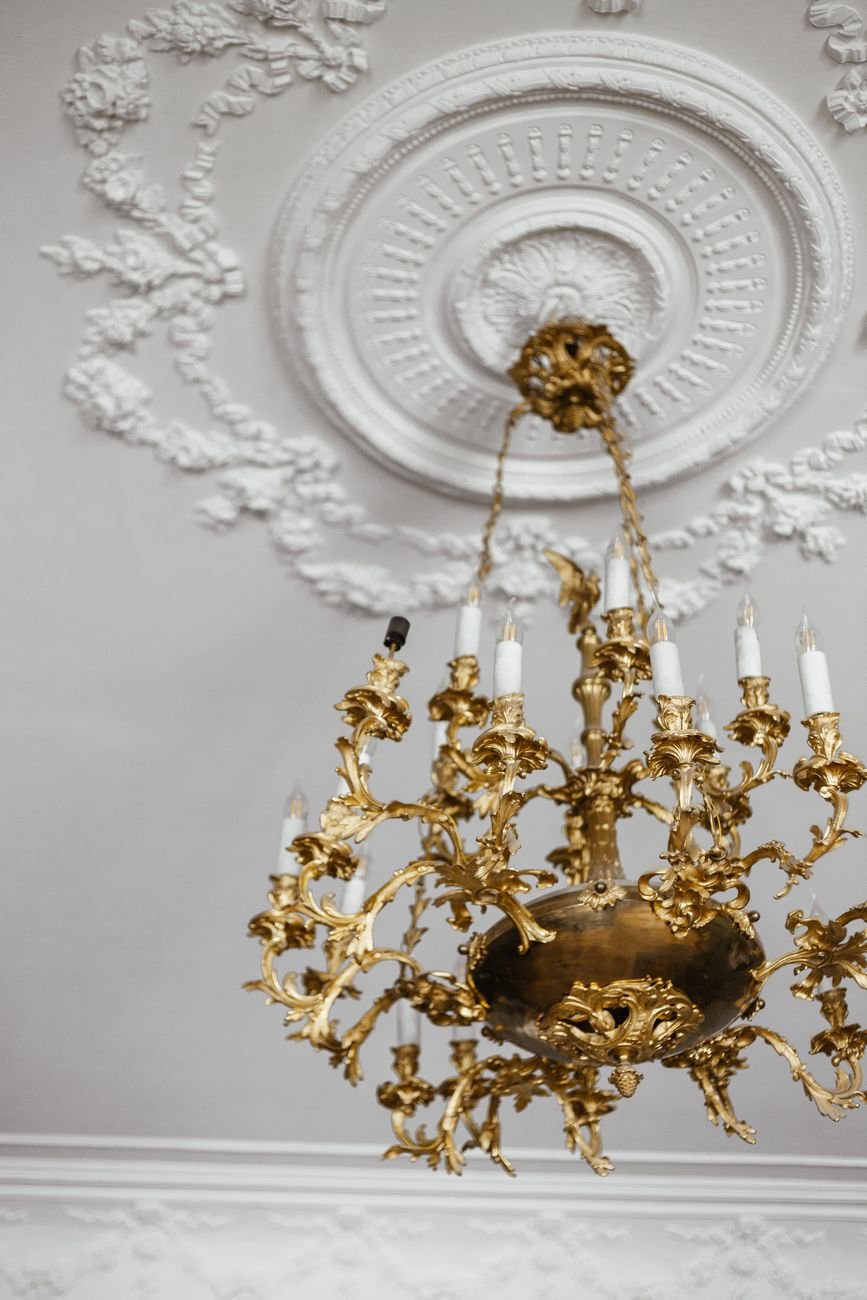 A luxurious gold chandelier suspended from an intricately designed white ceiling.